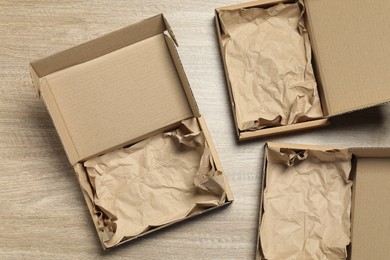 Photo of Open cardboard boxes with crumpled paper on wooden background, flat lay. Packaging goods
