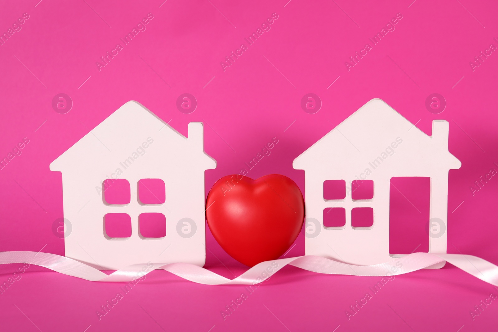 Photo of White ribbon and decorative heart between two house models on pink background symbolizing connection in long-distance relationship