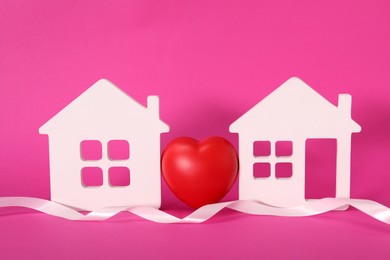 Photo of White ribbon and decorative heart between two house models on pink background symbolizing connection in long-distance relationship