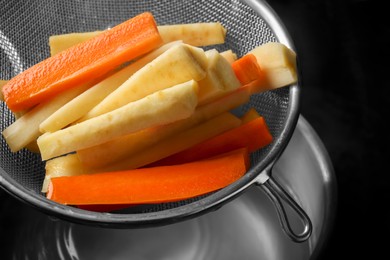 Sieve with cut parsnips and carrots over pot of water, closeup