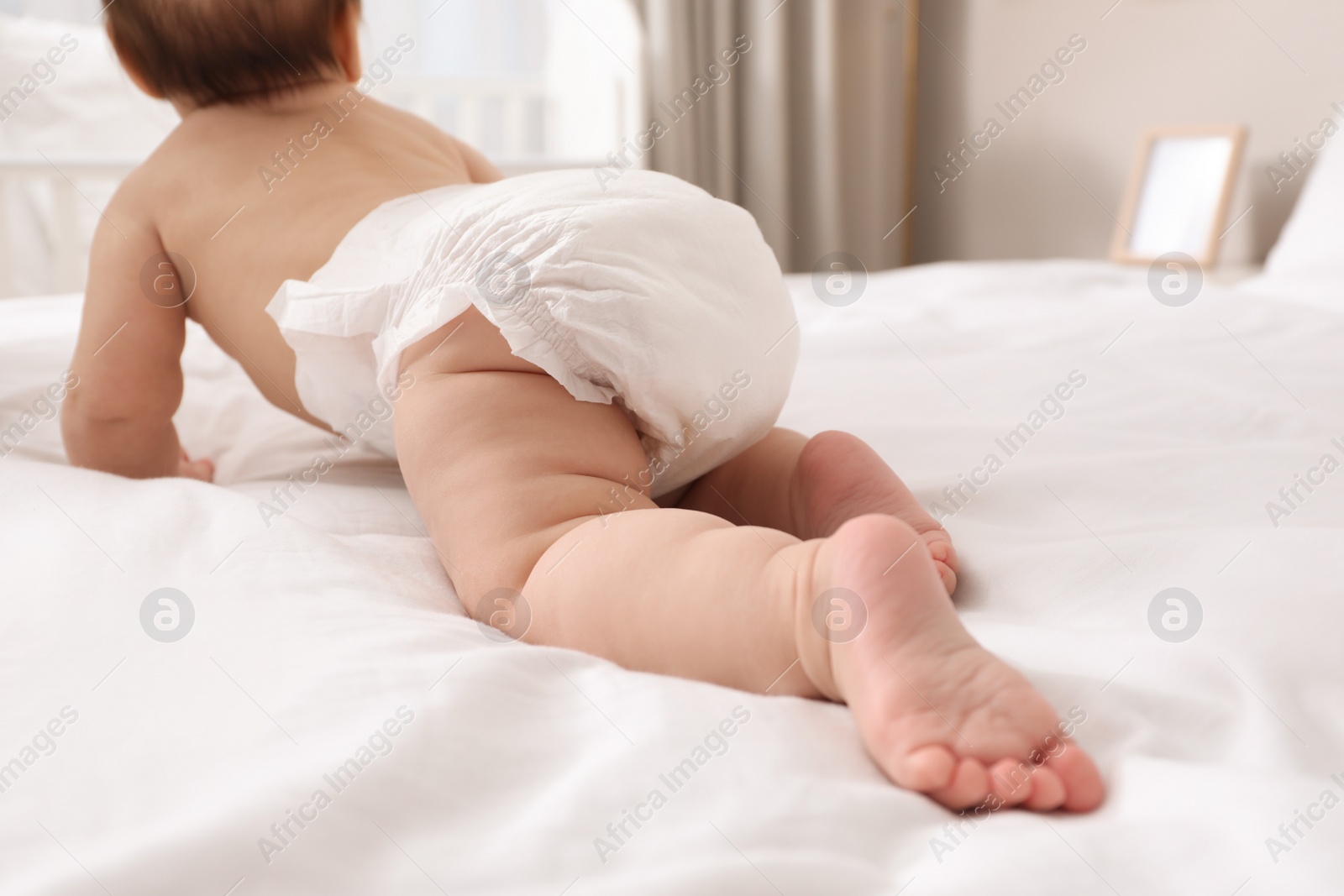 Photo of Little baby in diaper on bed at home, back view