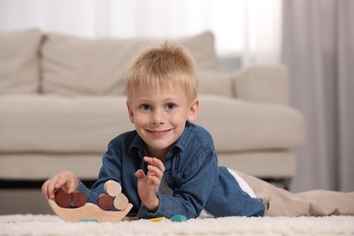 Photo of Cute little boy playing with wooden balance toy on carpet indoors