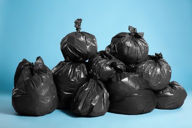 Photo of Black trash bags full of garbage on light blue background