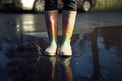 Photo of Woman with bright rubber boots in puddle, closeup. Rainy weather