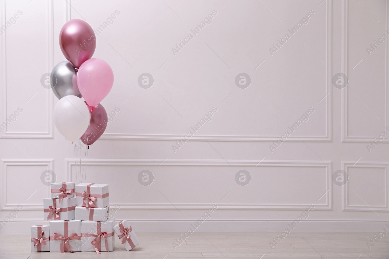 Photo of Many gift boxes and balloons near white wall in room. Space for text