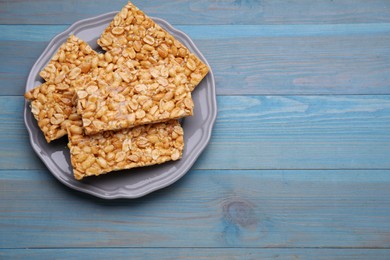 Photo of Delicious peanut bars (kozinaki) on light blue wooden table, top view. Space for text