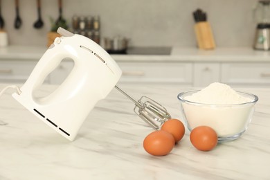 Modern mixer, eggs and bowl with flour on white marble table in kitchen