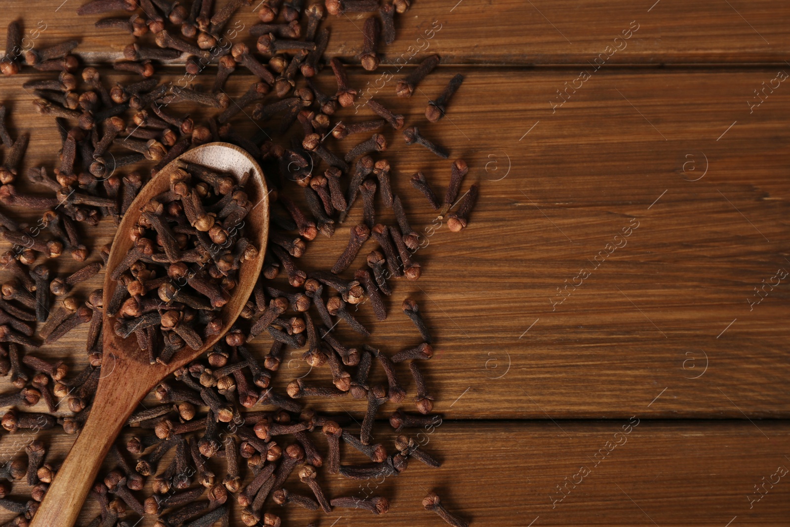 Photo of Pile of aromatic dry cloves and spoon on wooden table, flat lay. Space for text