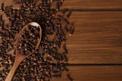 Photo of Pile of aromatic dry cloves and spoon on wooden table, flat lay. Space for text