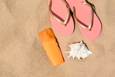 Photo of Bottle with sun protection spray, flip flops and seashell on sandy beach, flat lay. Space for text