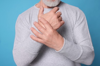 Photo of Senior man suffering from pain in hands on light blue background, closeup. Arthritis symptoms