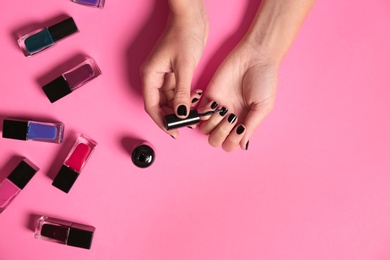 Woman applying nail polish on color background, top view