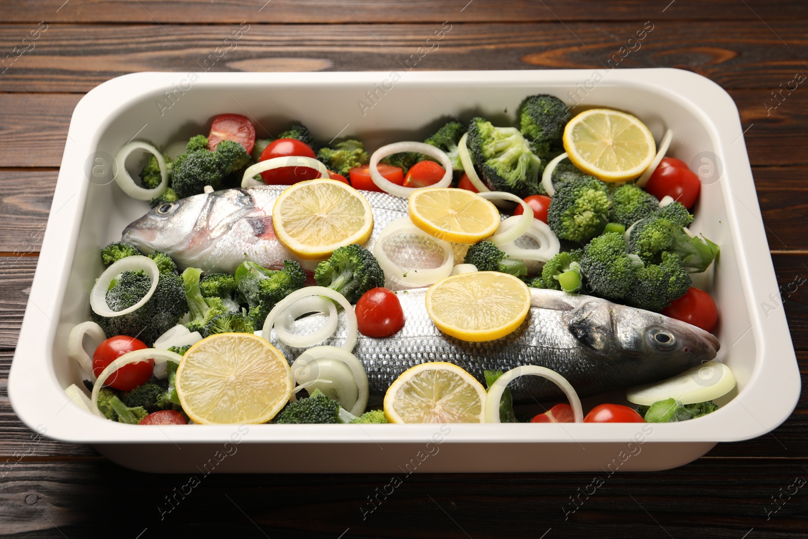 Photo of Raw fish with vegetables and lemon in baking dish on wooden table