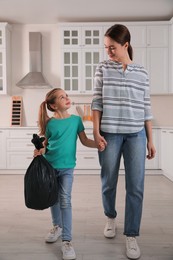 Photo of Little girl holding bin bag full of garbage in kitchen