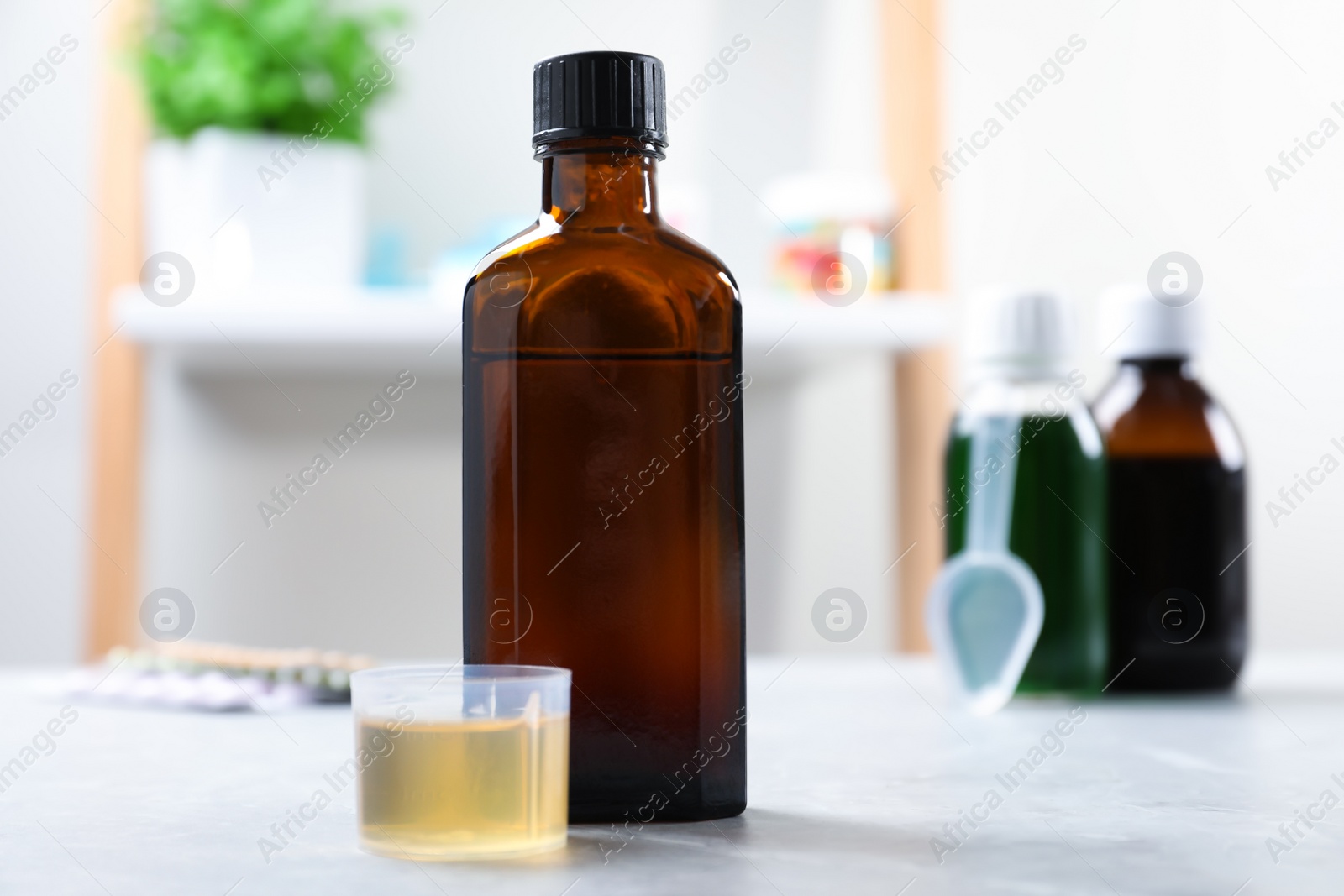 Photo of Bottle of syrup and measuring cup on white table. Cold medicine