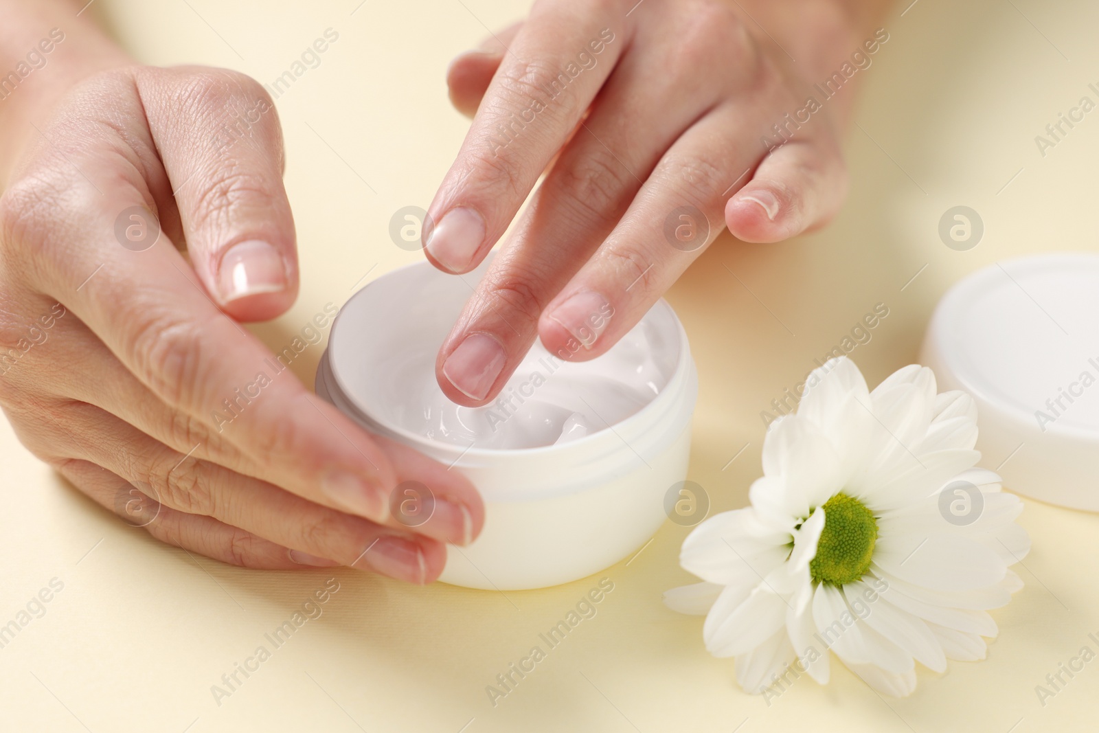 Photo of Woman with jar of hand cream and chamomile flower on beige background, closeup