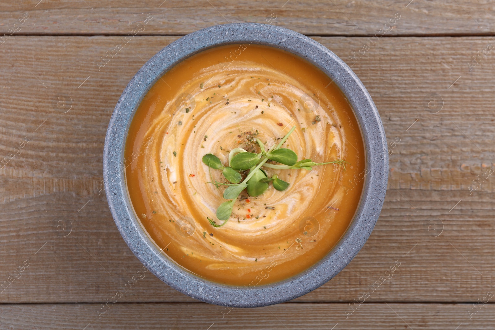 Photo of Bowl of delicious pumpkin soup with microgreens on wooden table, top view