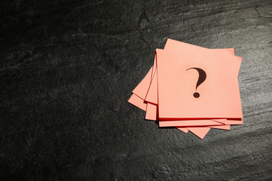 Photo of Pink paper cards with question mark on black stone table, top view. Space for text