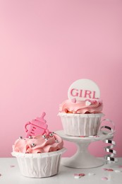 Baby shower cupcakes with toppers on white table against pink background, space for text