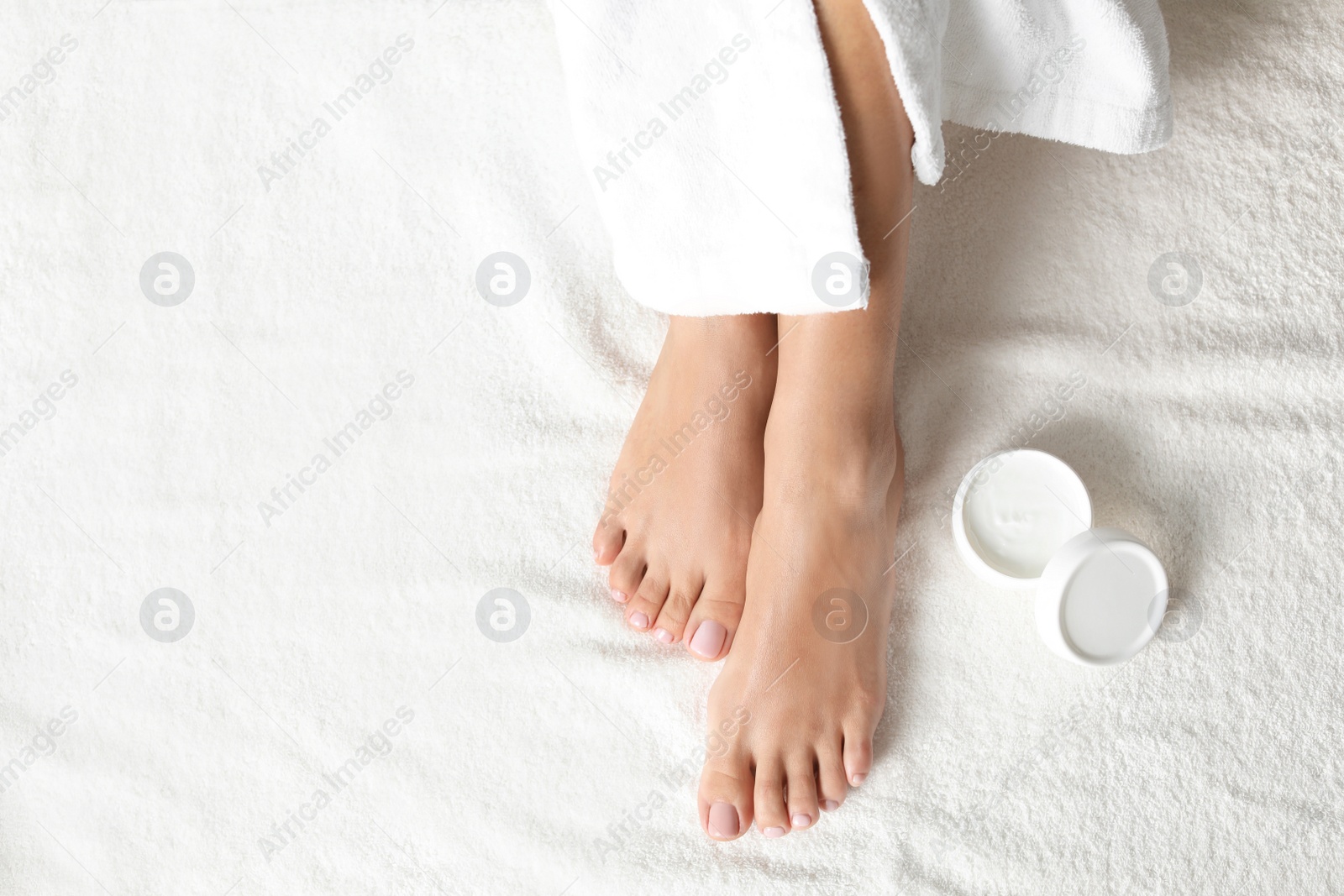 Photo of Top view of woman with beautiful feet and moisturizing cream on white towel, space for text. Spa treatment