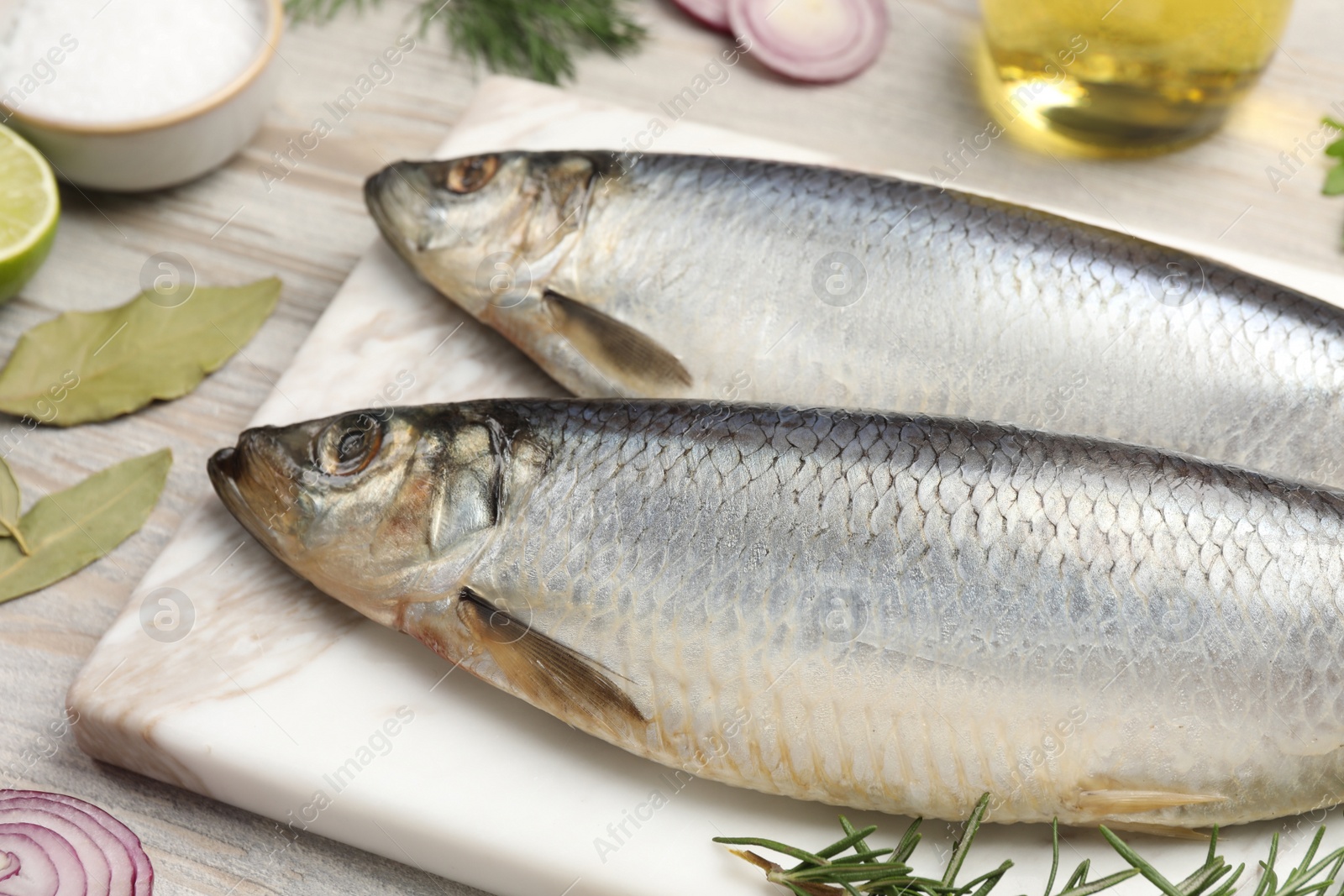 Photo of Delicious salted herrings and different ingredients on light wooden table, closeup