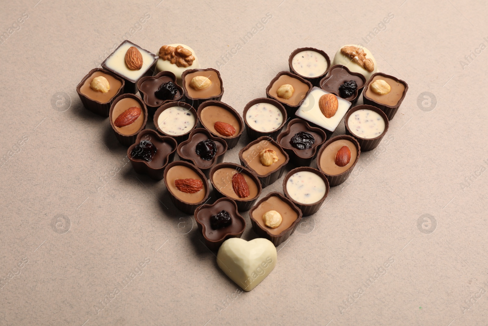 Photo of Heart made with delicious chocolate candies on beige background, above view