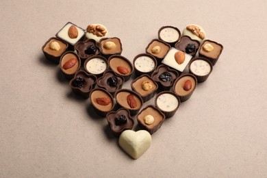Heart made with delicious chocolate candies on beige background, above view