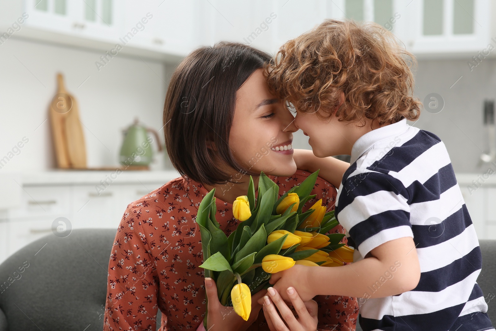 Photo of Little son congratulating his mom with Mother`s day at home. Woman holding bouquet of yellow tulips