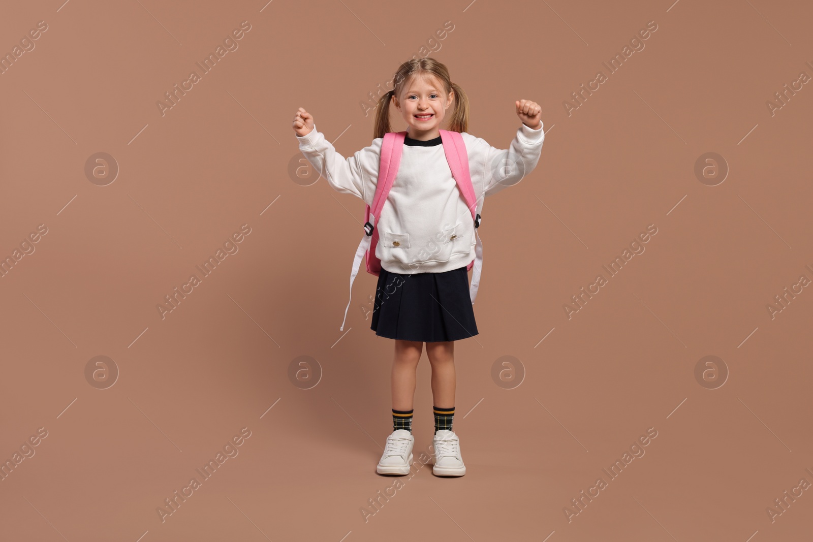 Photo of Happy schoolgirl with backpack on brown background