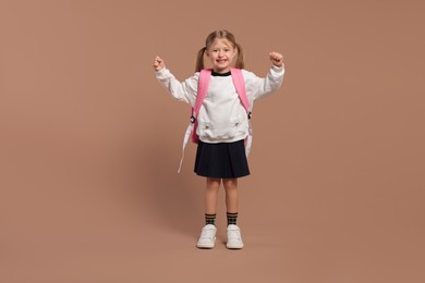 Happy schoolgirl with backpack on brown background