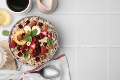 Photo of Oatmeal with freeze dried fruits, nuts and mint on white tiled table, flat lay. Space for text