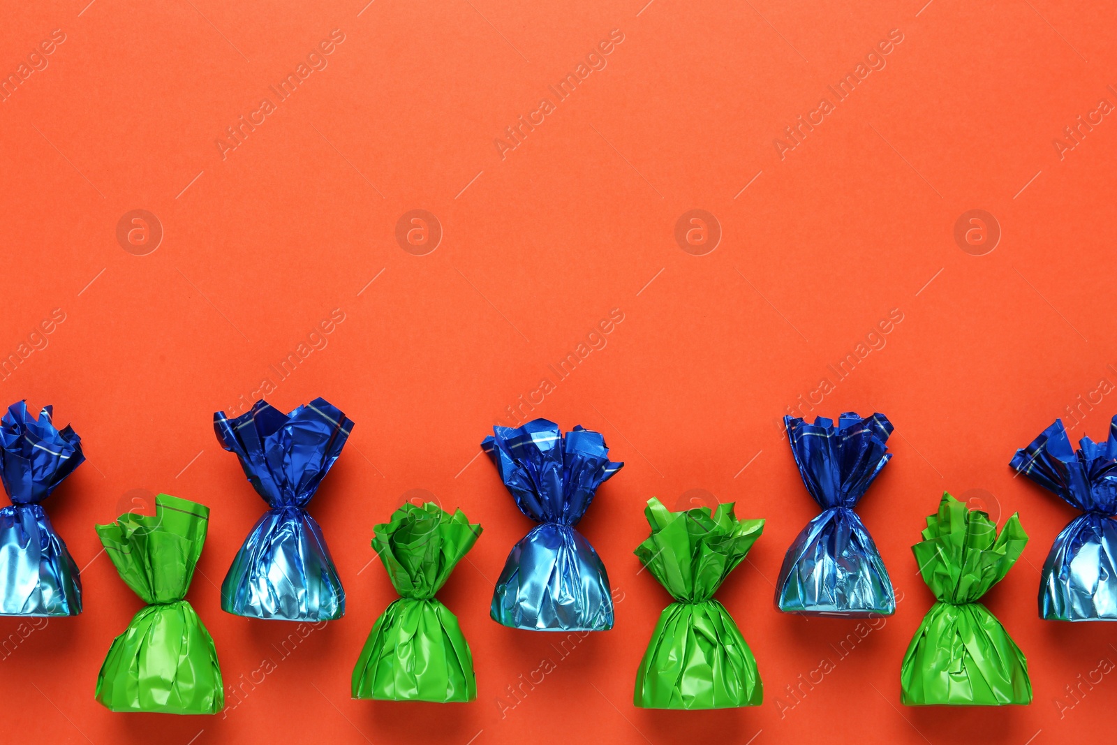 Photo of Many candies in colorful wrappers on orange background, flat lay. Space for text