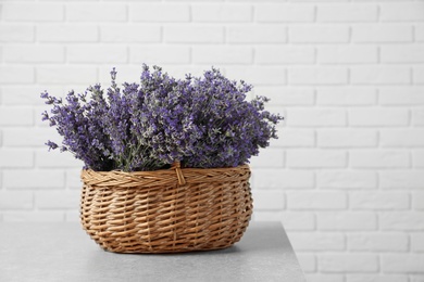 Fresh lavender flowers in basket on stone table against white brick wall, space for text