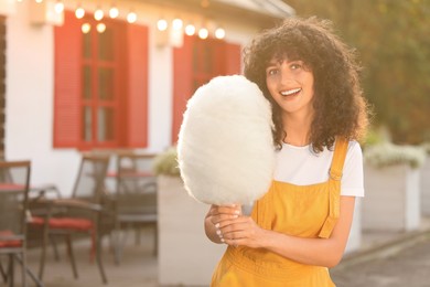 Photo of Happy woman with cotton candy outdoors on sunny day. Space for text