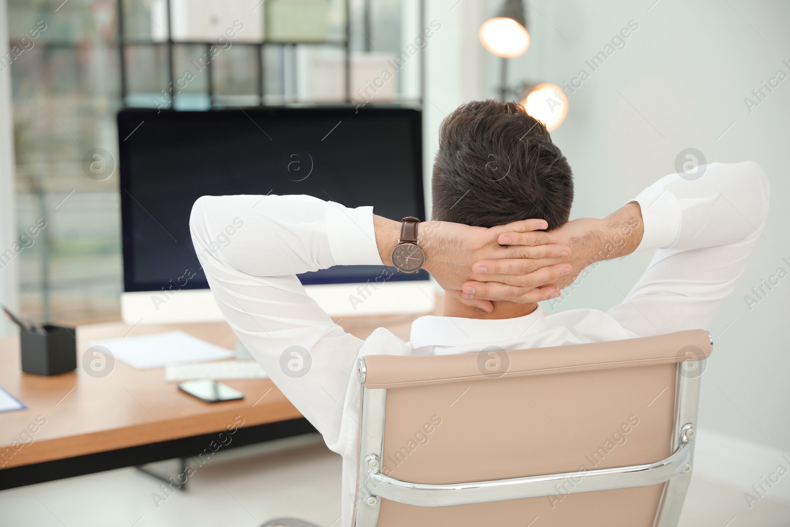 Photo of Young businessman relaxing in office chair at workplace, back view