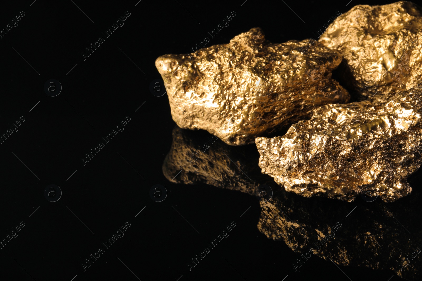 Photo of Gold nuggets on black reflective surface, space for text