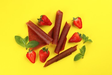 Photo of Delicious fruit leather rolls, mint and strawberries on yellow background, flat lay