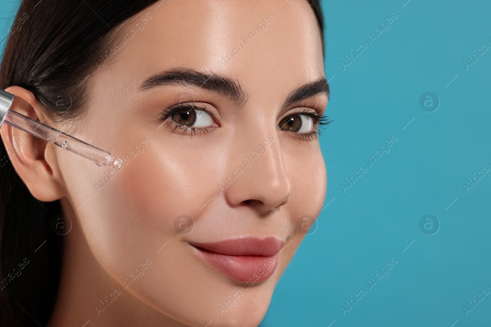 Photo of Beautiful young woman applying serum onto her face on light blue background, closeup. Space for text