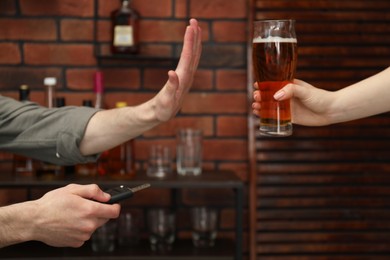 Photo of Man with car keys refusing from alcohol while woman suggesting him beer in bar, closeup. Don't drink and drive concept