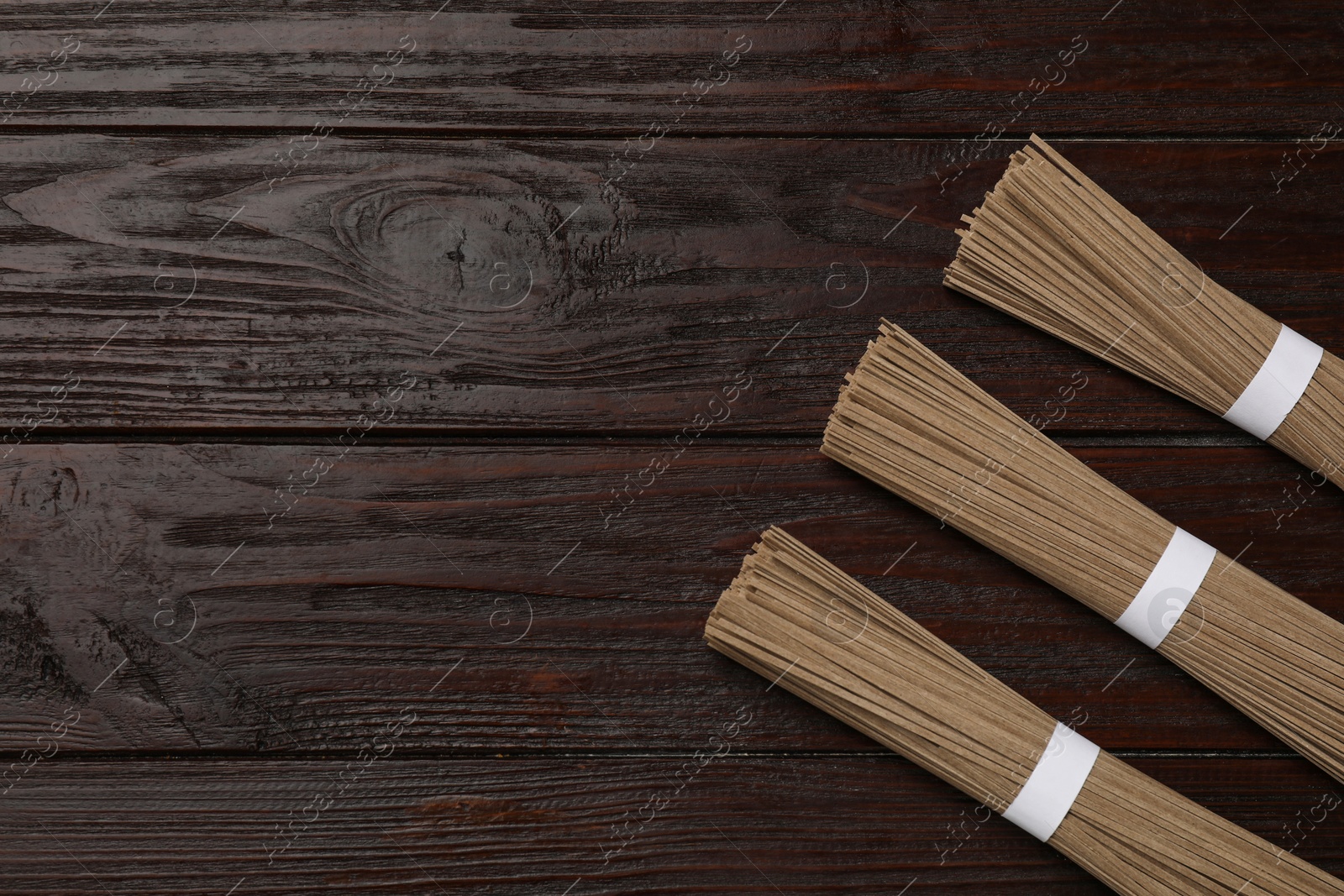 Photo of Uncooked buckwheat noodles (soba) on wooden table, flat lay. Space for text