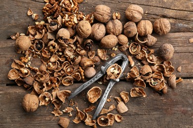 Photo of Walnuts, pieces of shells and nutcracker on wooden table, flat lay