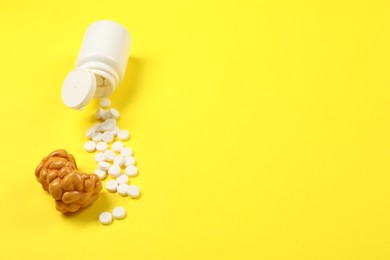 Photo of Endocrinology. Bottle with pills and model of thyroid gland on yellow background, above view. Space for text