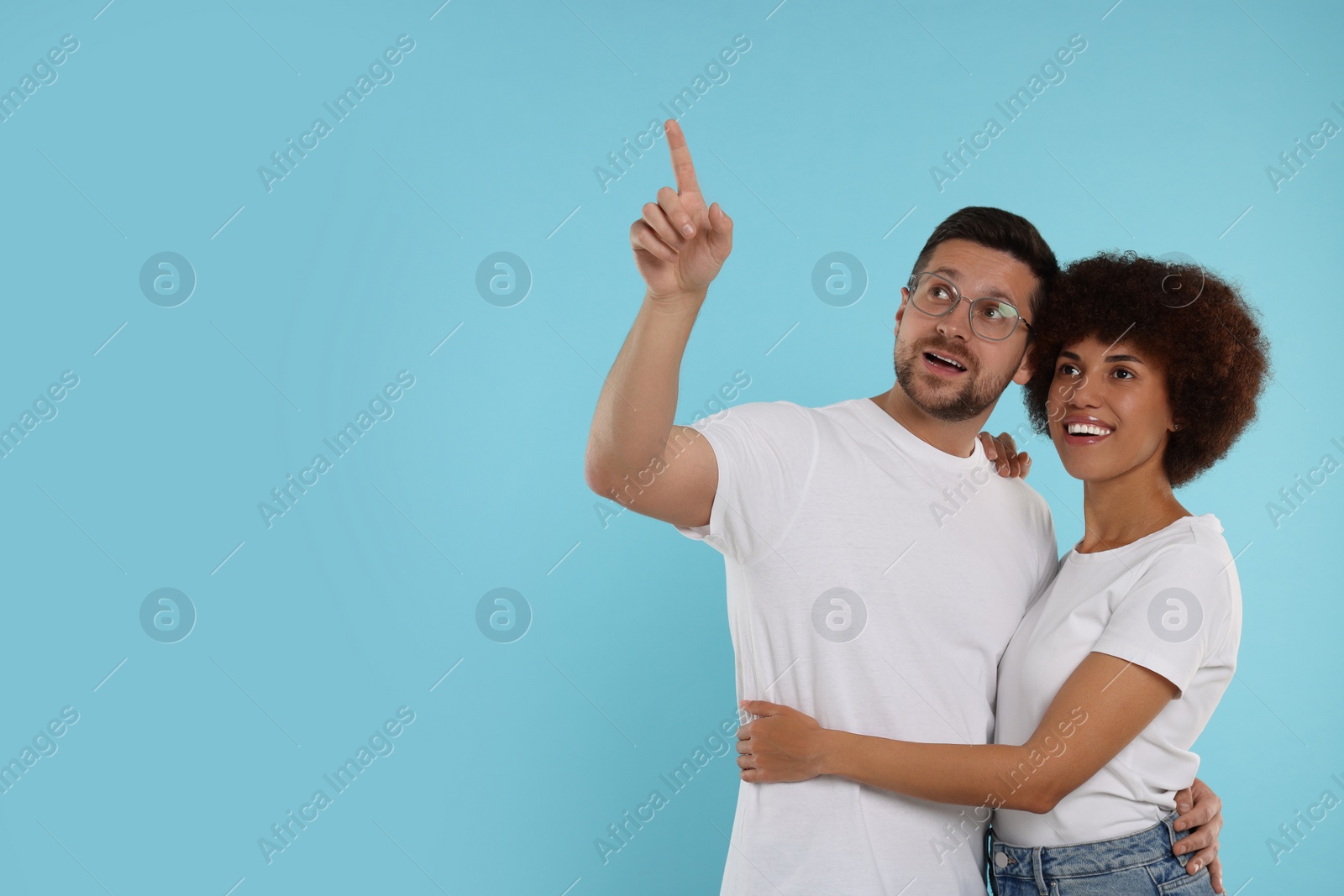 Photo of International dating. Lovely couple pointing at something on light blue background, space for text
