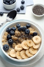 Photo of Tasty oatmeal with banana, blueberries and chia seeds served in bowl on white wooden table, above view