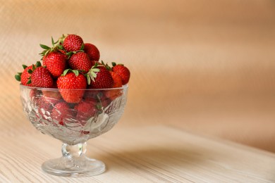 Photo of Glass dessert bowl with ripe strawberries on white wooden table. Space for text