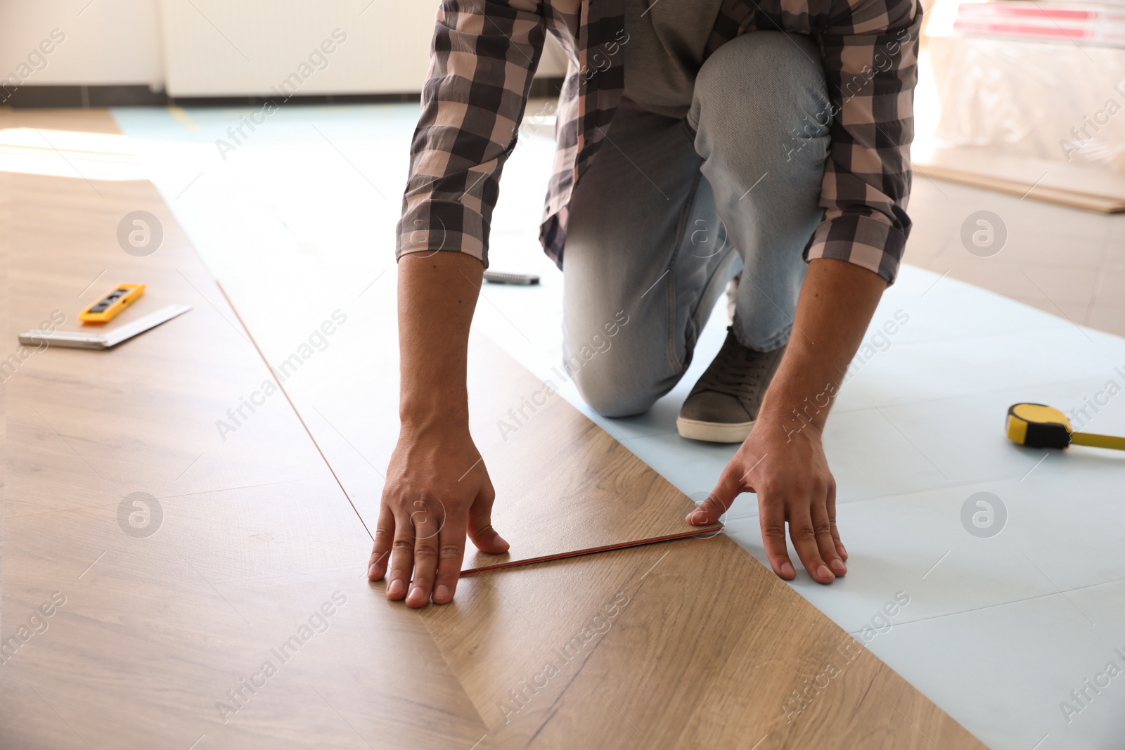 Photo of Worker installing laminated wooden floor indoors, closeup