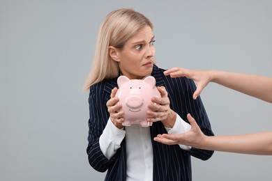 Photo of Scammer taking piggy bank from scared woman on grey background. Be careful - fraud