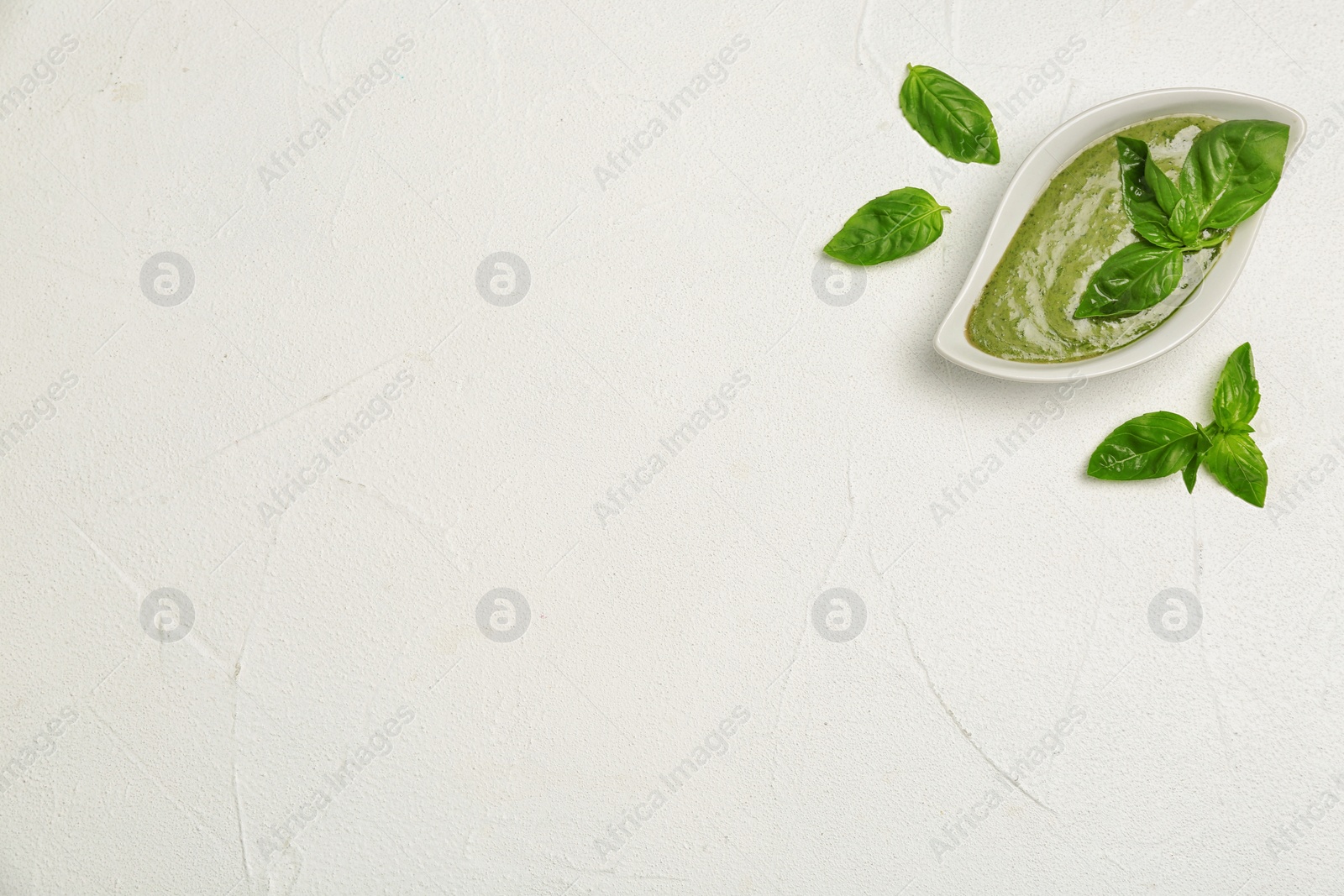 Photo of Sauce in gravy boat and basil leaves on white table, top view with space for text