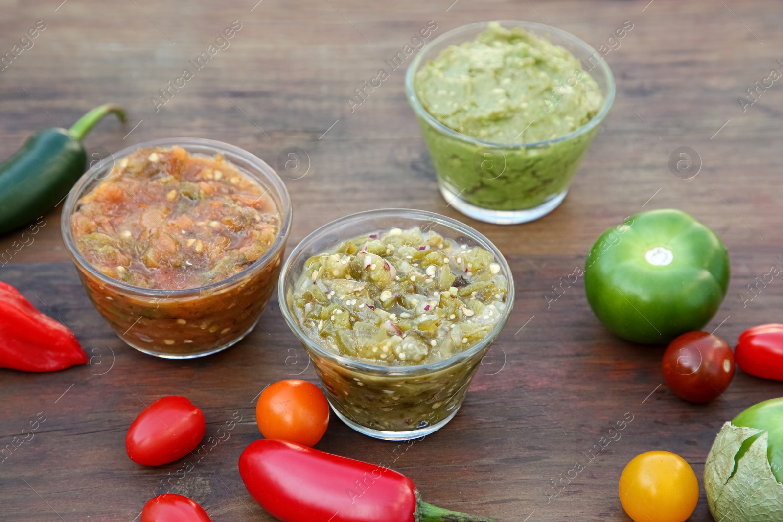 Photo of Tasty salsa sauces and ingredients on wooden table