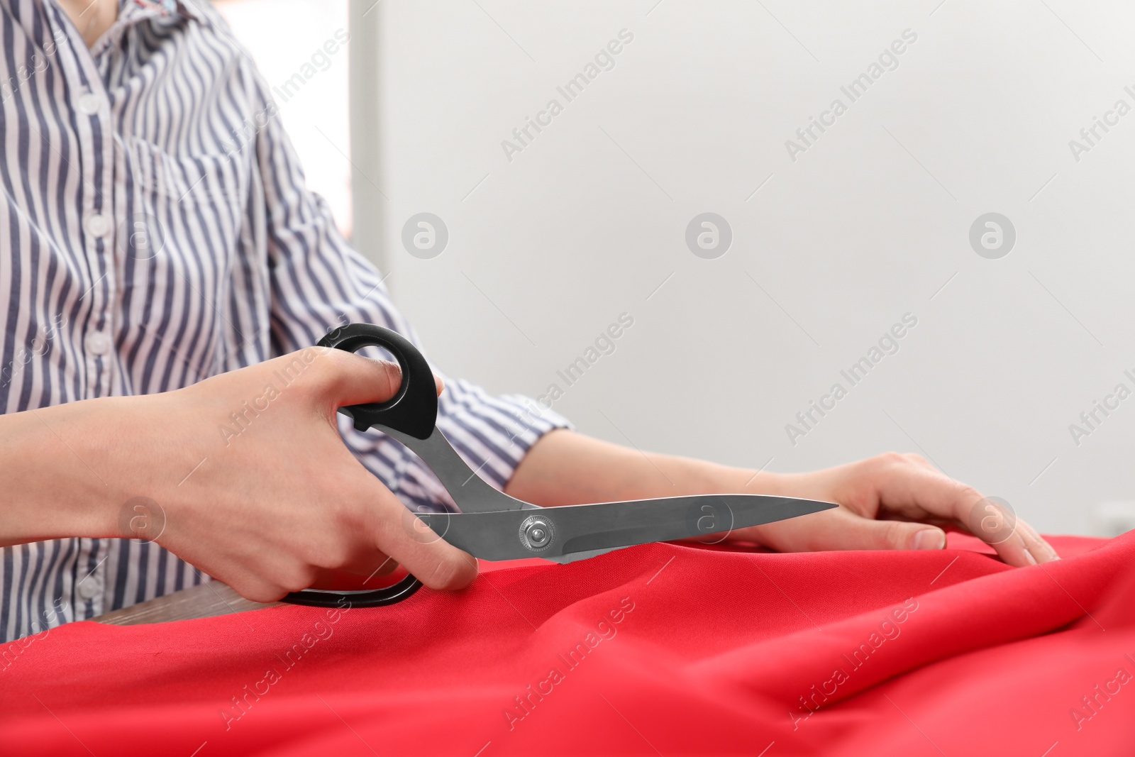 Photo of Woman cutting fabric with sharp scissors at table, closeup. Space for text